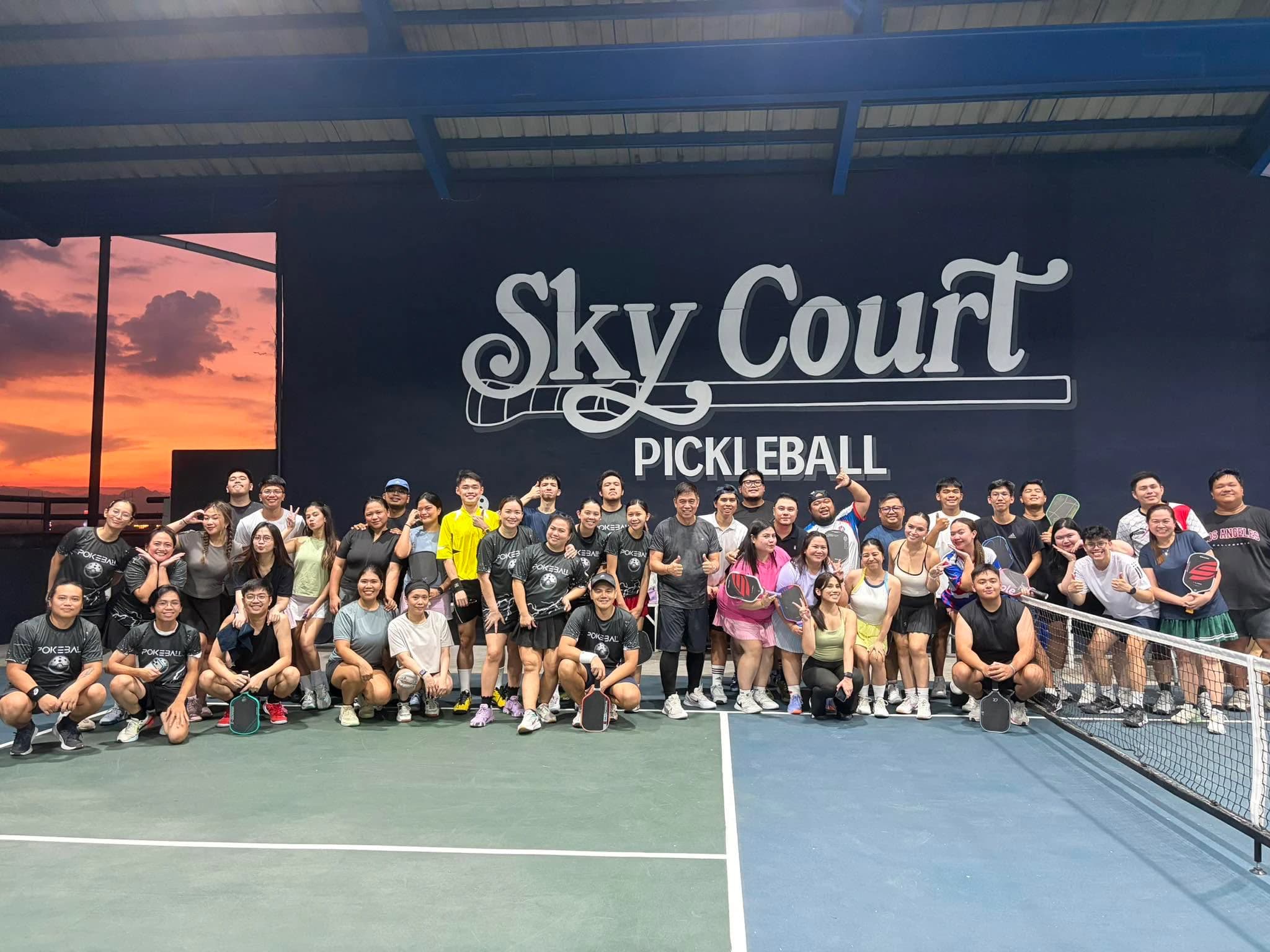 SkyCourt community players gather on the rooftop court beneath the venue logo at sunset.