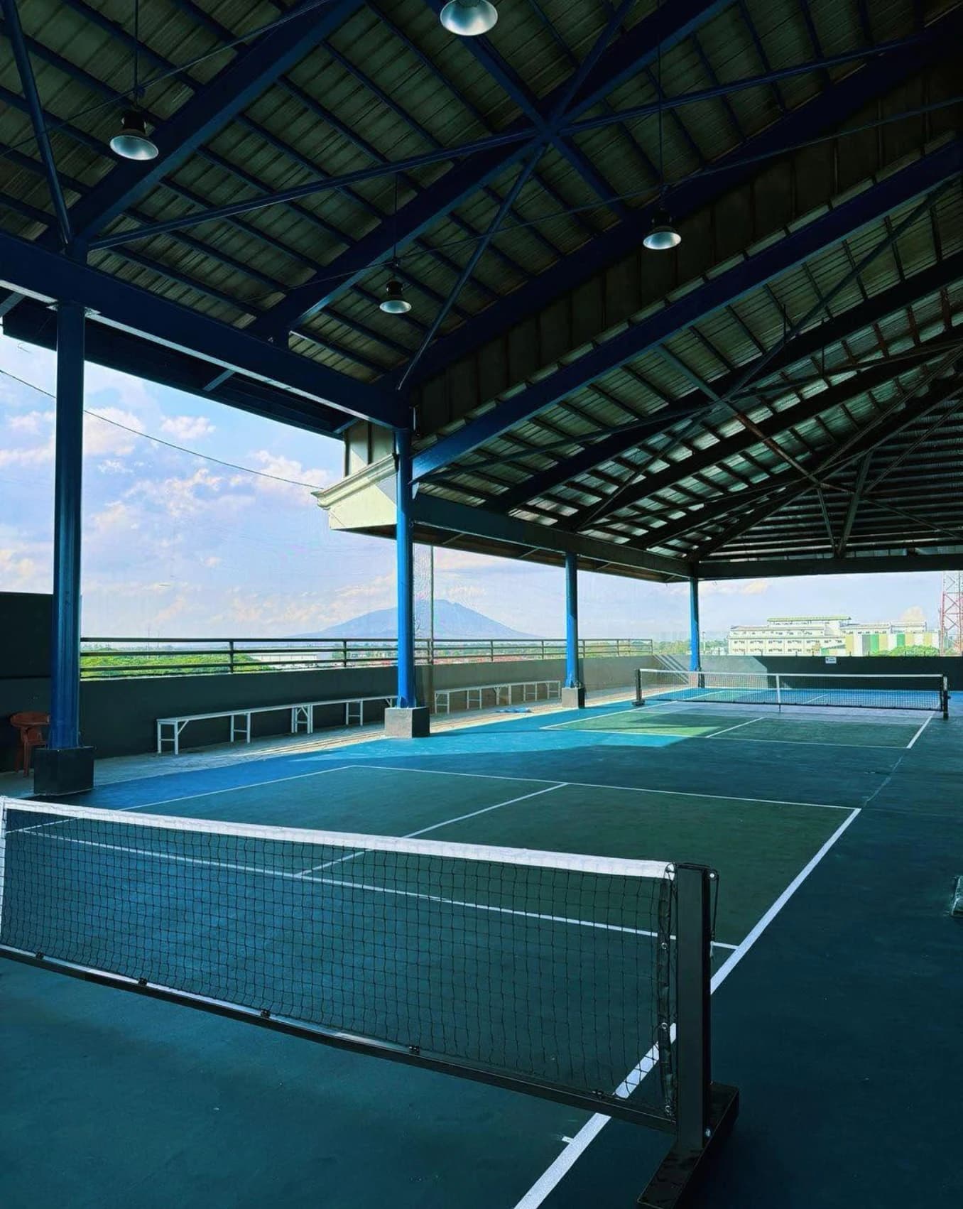 Blue and green rooftop pickleball courts beneath a covered roof with mountains in the distance.